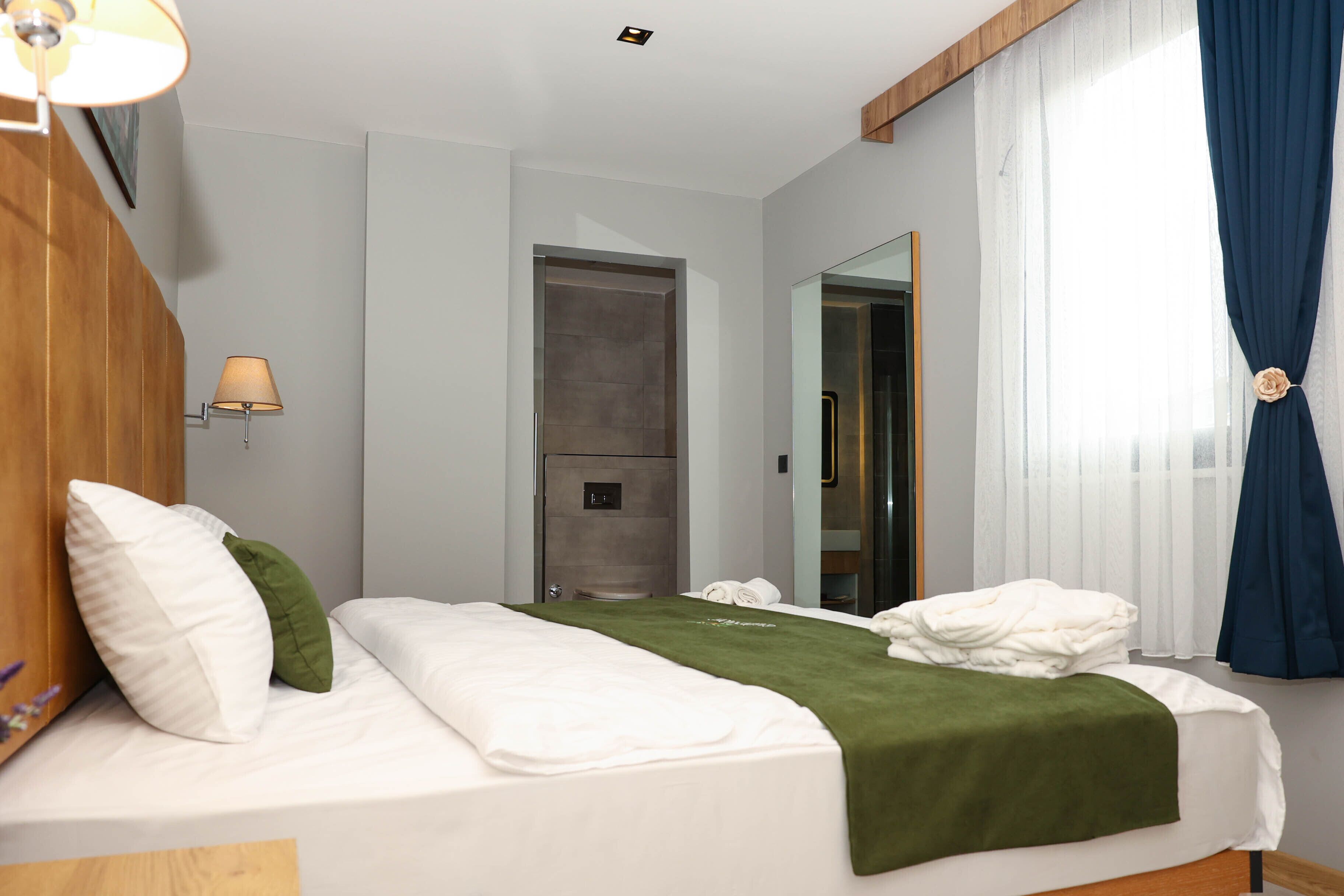 A hotel room with a bed, a lamp, a door, and a window with curtains.