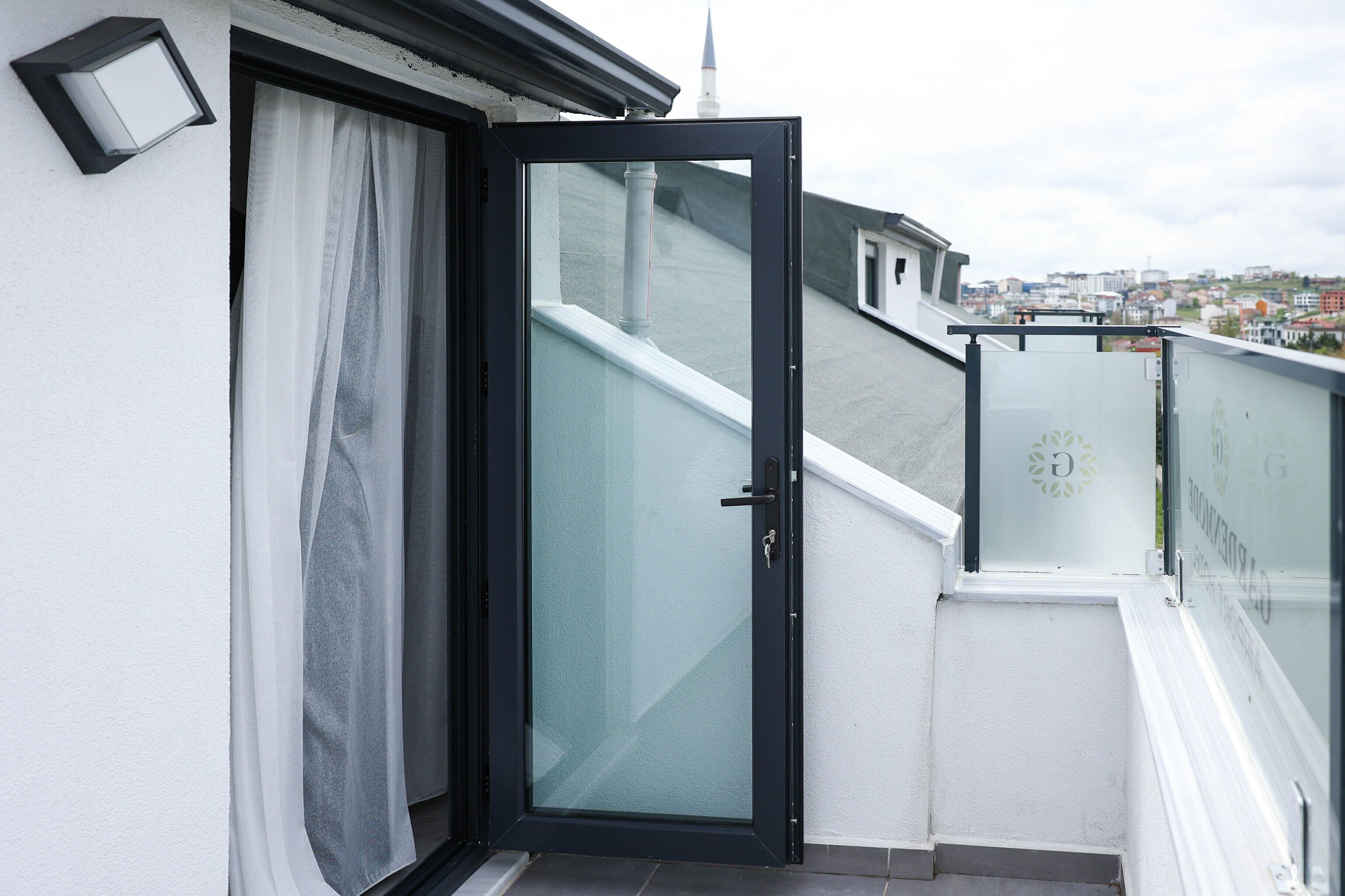 A balcony with a glass door, white walls, and a view of a cityscape.