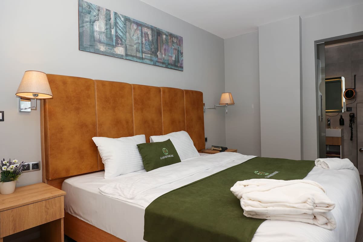 Una habitación de hotel con una cama grande, cabecera de madera, una manta verde y un cuadro en la pared.