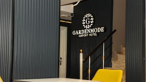 A modern interior with a staircase, a sign for 'Gardenmode Airport Hotel', and a table with chairs. - Garden Mode Airport Hotel (Arnavutköy)