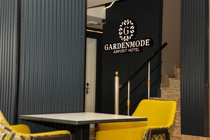 Un interior moderno con una escalera, un letrero que dice 'Gardenmode Airport Hotel' y una mesa con sillas.