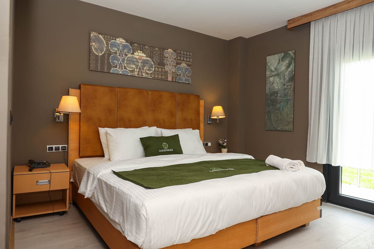 Una cama bien hecha con un plaid verde, dos lámparas de noche y una mesita de noche con un teléfono y un cargador.