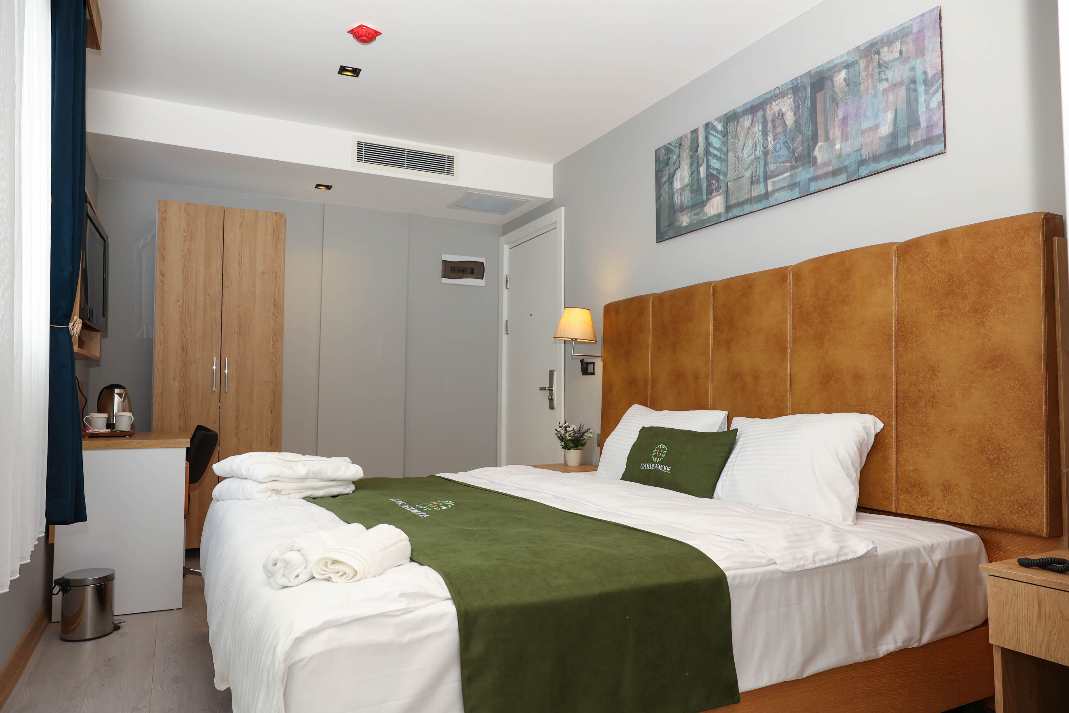 A hotel room with a bed, a desk, a wardrobe, and a painting on the wall.