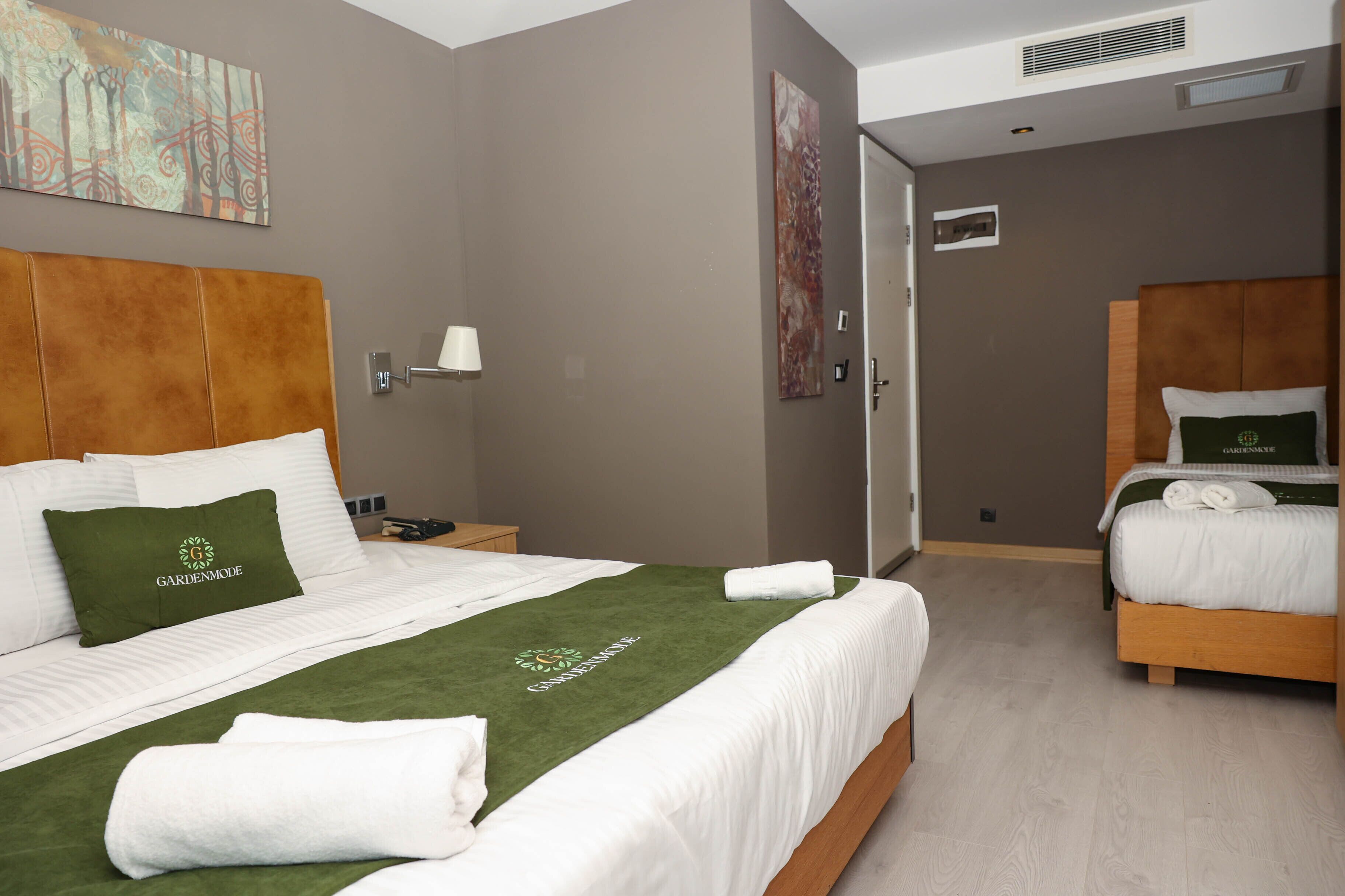 Una habitación de hotel con una cama grande, una cama más pequeña, una mesita de noche, una lámpara y obras de arte en las paredes.