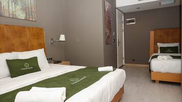Una habitación de hotel con una cama grande, una cama más pequeña, una mesita de noche, una lámpara y obras de arte en las paredes.