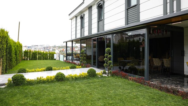 A modern building with a well-maintained garden, large windows, and a view of the cityscape. - Garden Mode Airport Hotel (Arnavutköy)