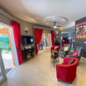 A living room with red and grey furniture, a TV, and a ceiling fan. - Résidence du Port Villa N° 04 Avec Piscine Face à la mer (Saly)