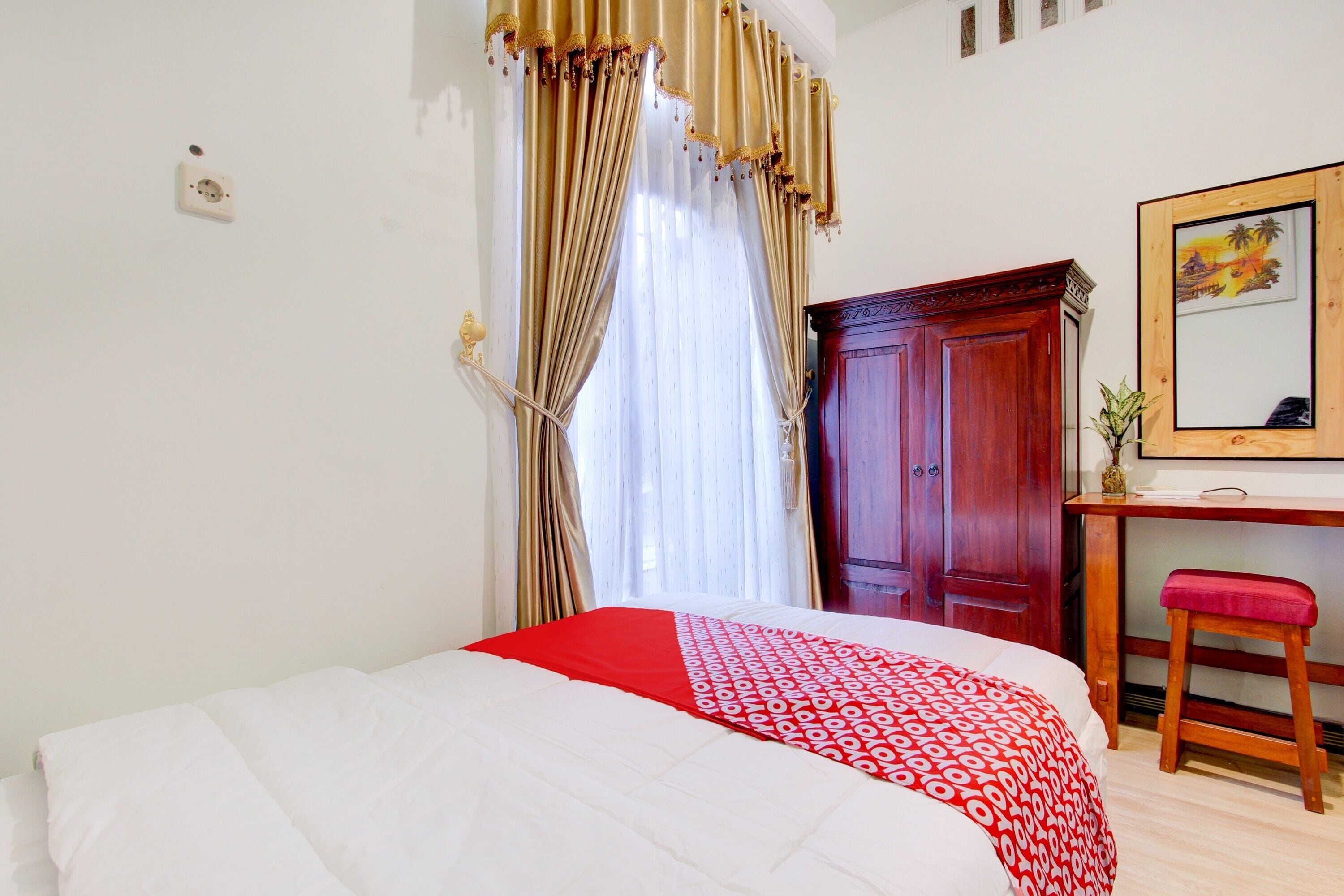 Un dormitorio con cama, un escritorio de madera, una silla roja, un armario y un espejo en la pared.