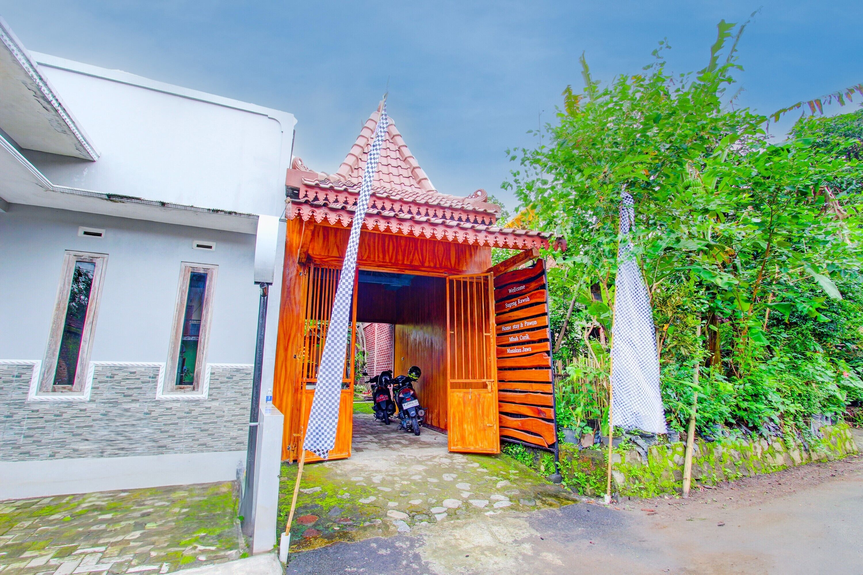 Una casa tradicional con techo de tejas rojas, un portón de madera y una motocicleta estacionada dentro.
