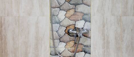 A shower with a stone mosaic wall and a handheld showerhead.