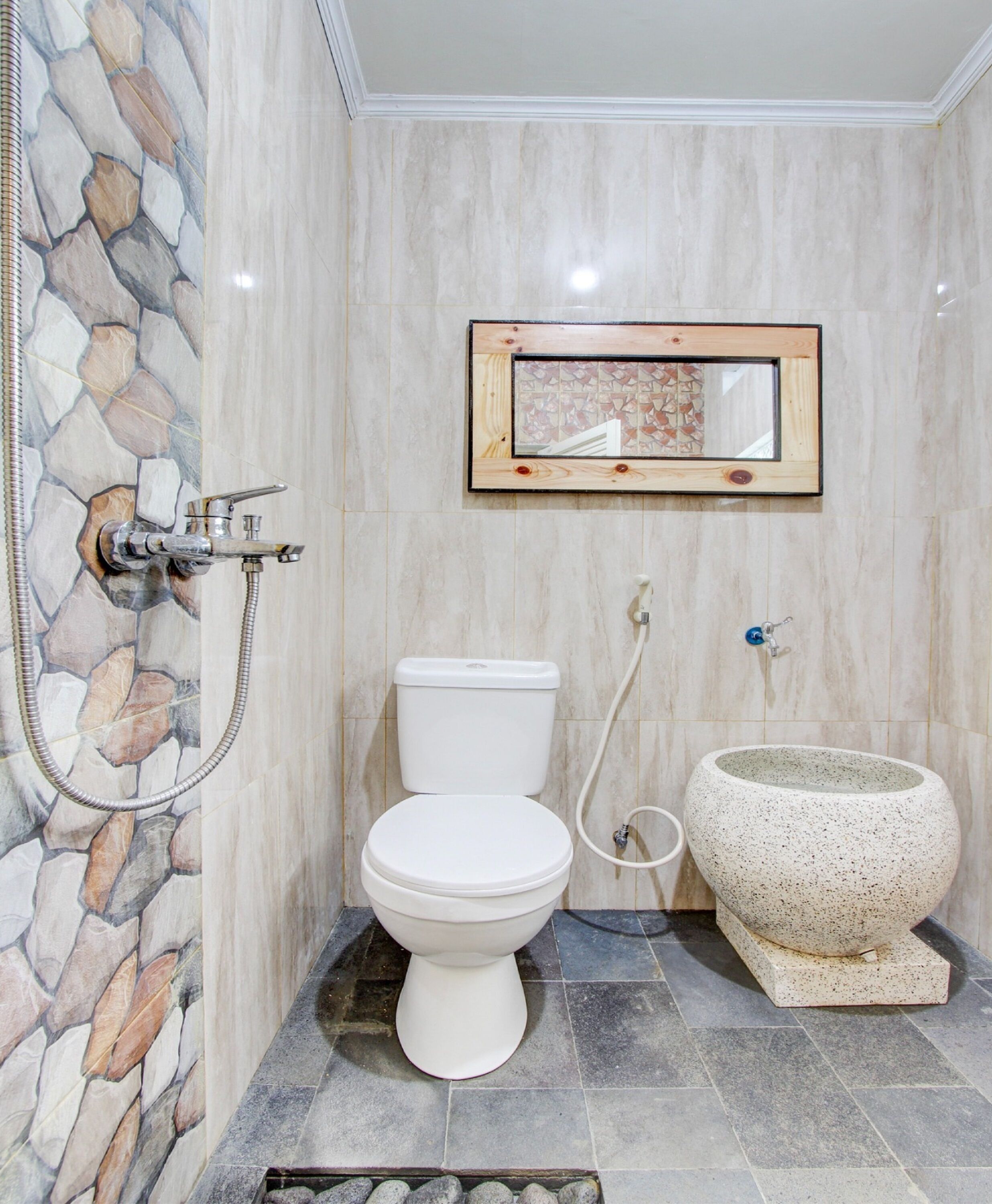 A bathroom with a stone wall, a toilet, a shower, and a sink with a bowl.