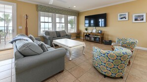 A living room with a grey sofa, a patterned armchair, a white coffee table, and a bookshelf. - Oceanfront 5 BR Beach House with a Private Pool! 19th Hole (Surfside Beach)