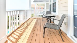 A wooden deck with a white railing, two wicker chairs, and a small round table. - Oceanfront 5 BR Beach House with a Private Pool! 19th Hole (Surfside Beach)