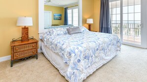A bedroom with a large bed, two bedside tables with lamps, a mirror, and a view of the outdoors through a sliding glass door. - Oceanfront 5 BR Beach House with a Private Pool! 19th Hole (Surfside Beach)