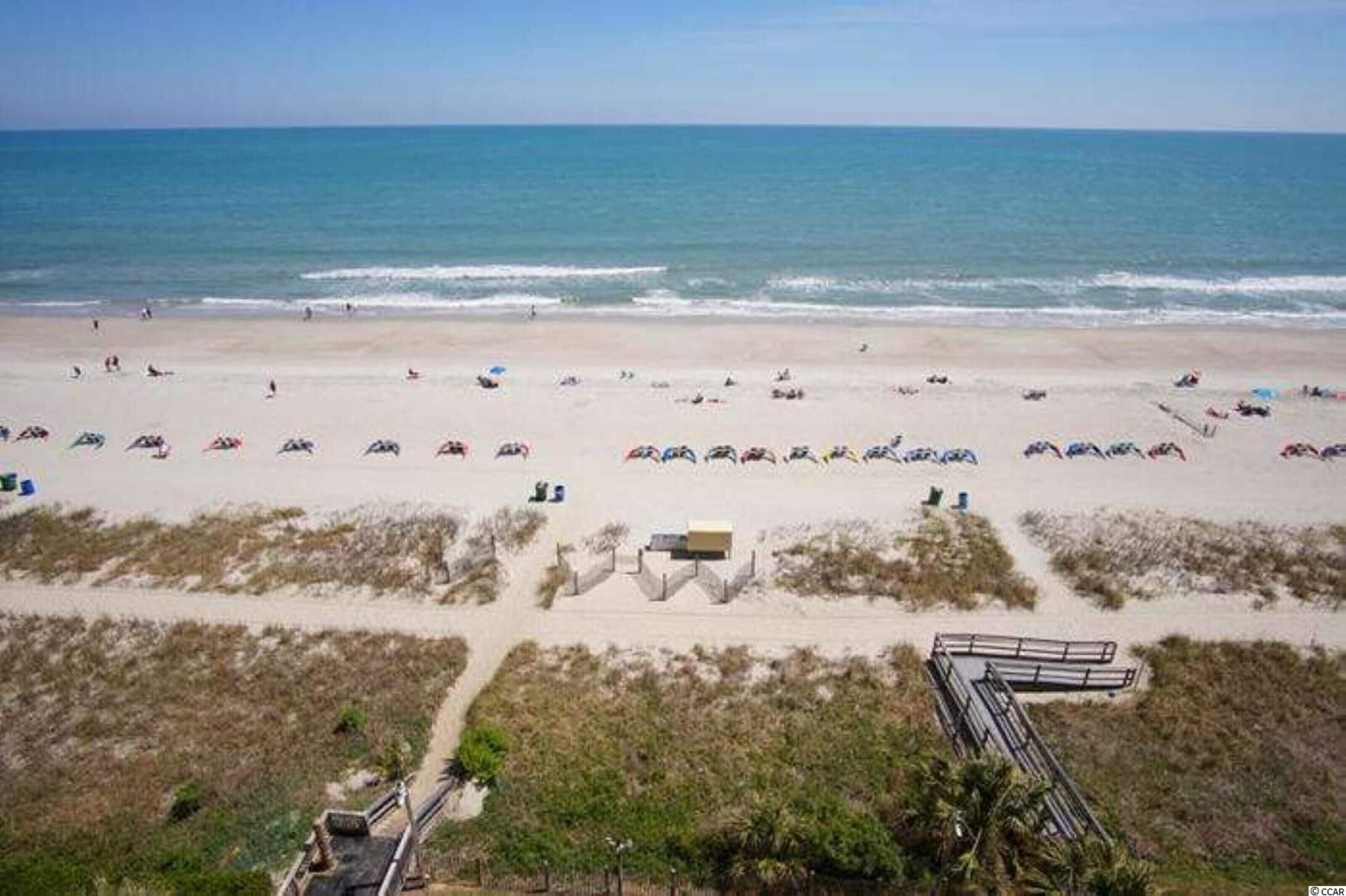 A beach with people and umbrellas, a sandy area, and a structure in the foreground.