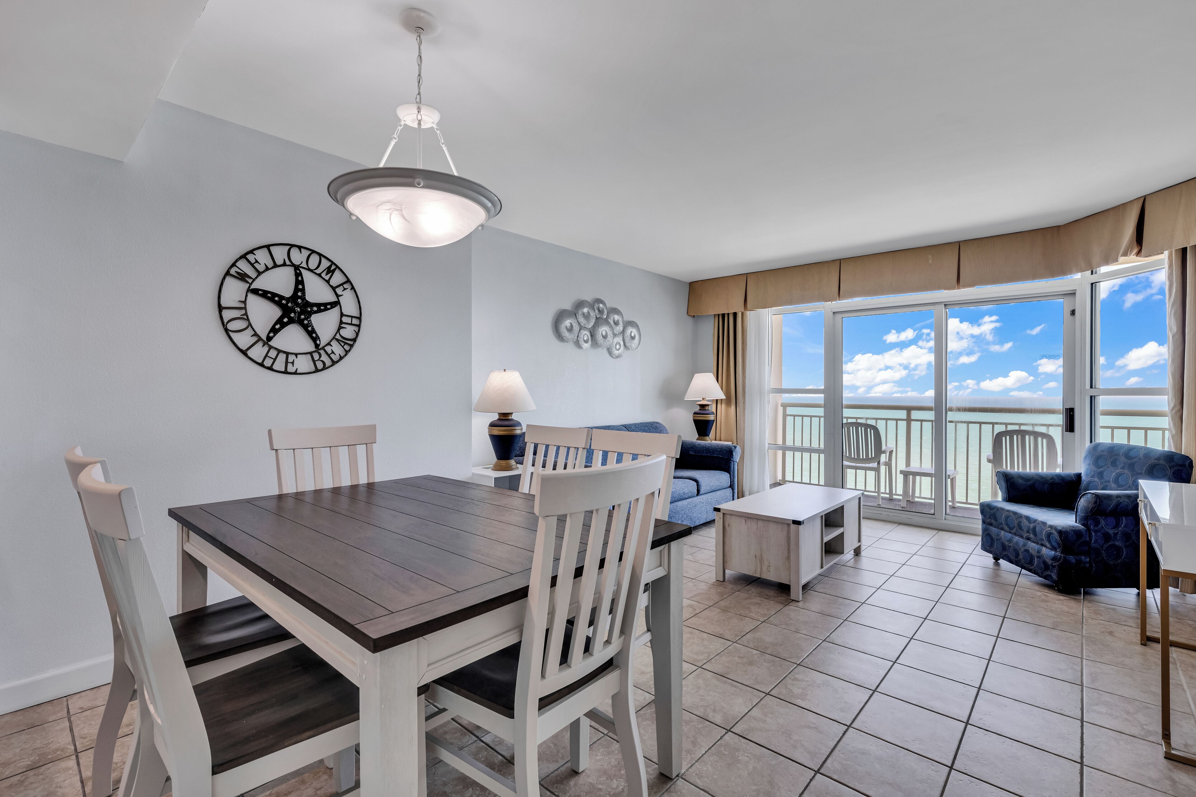 A dining area with a table and chairs, a sofa, and a balcony with a view.