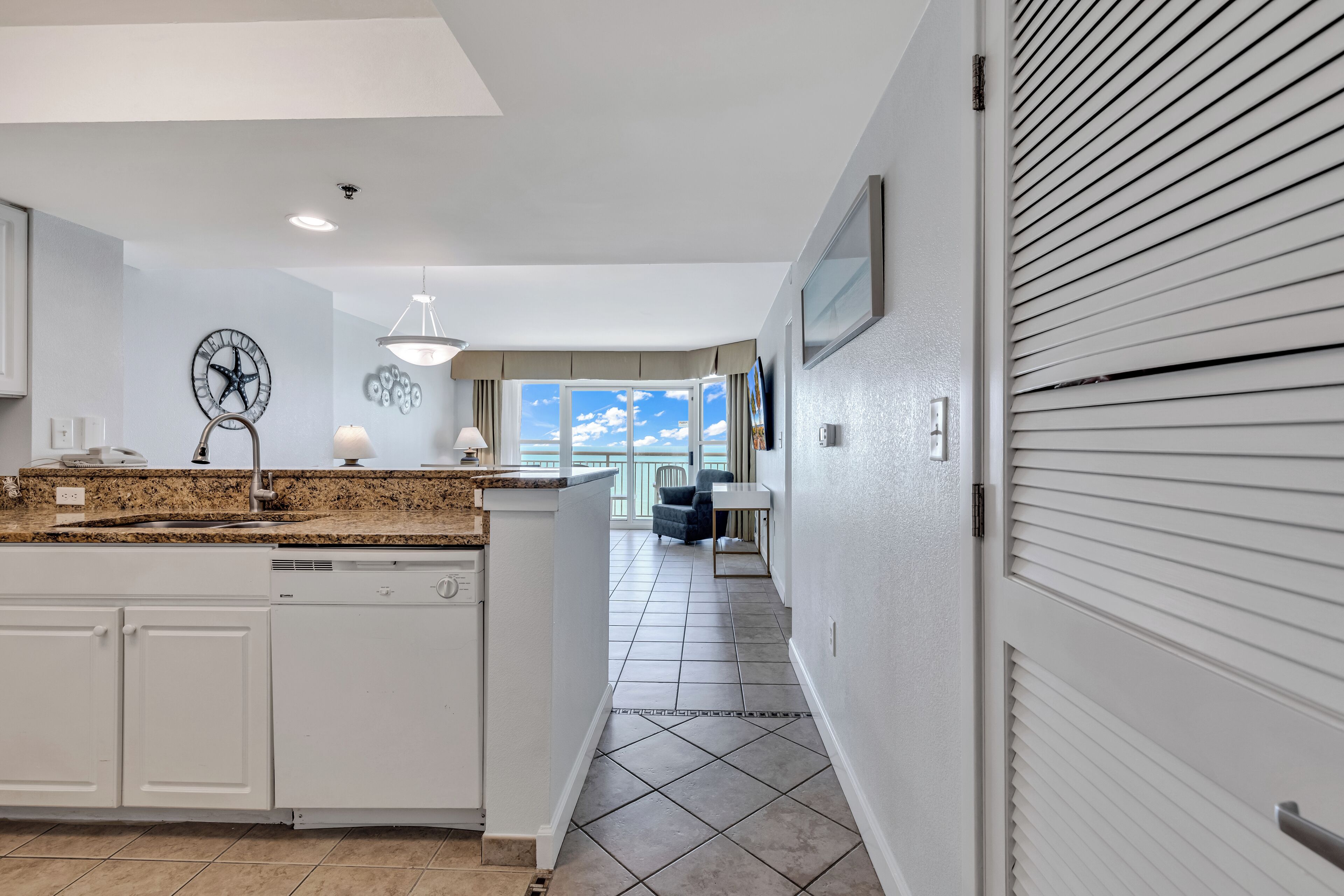 A modern kitchen with white cabinetry, a granite countertop, and a large window providing a view of the outdoors.
