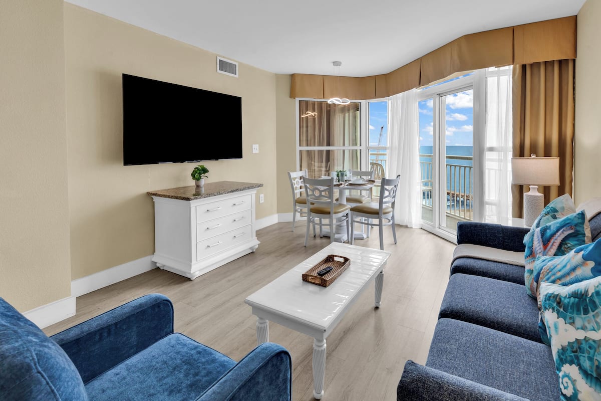 Un salon équipé d’un téléviseur à écran plat, un coin repas avec des chaises et une table, un canapé et un balcon avec vue.