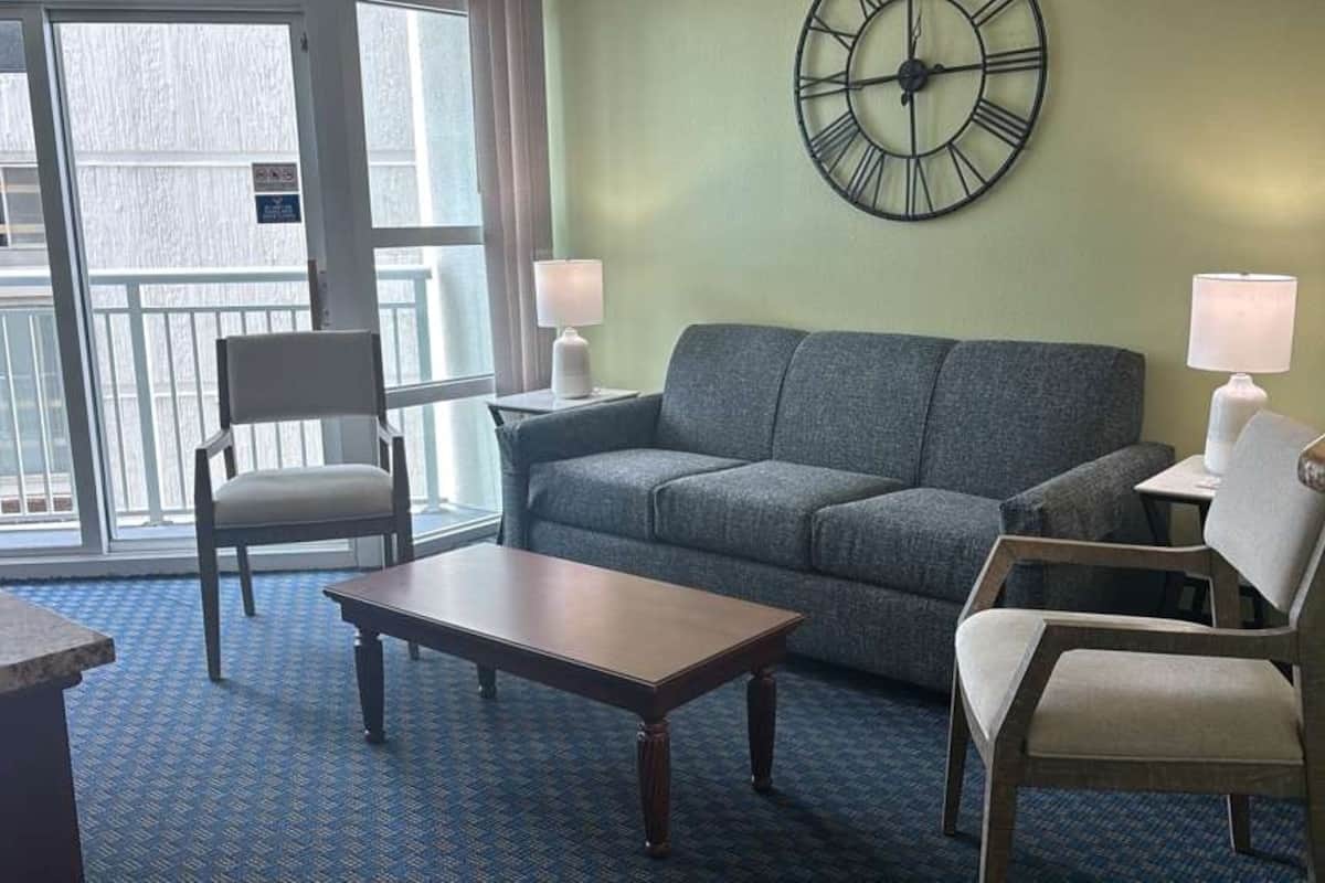 Une pièce comprenant un canapé, deux fauteuils, une table, une horloge et une fenêtre donnant sur un paysage.