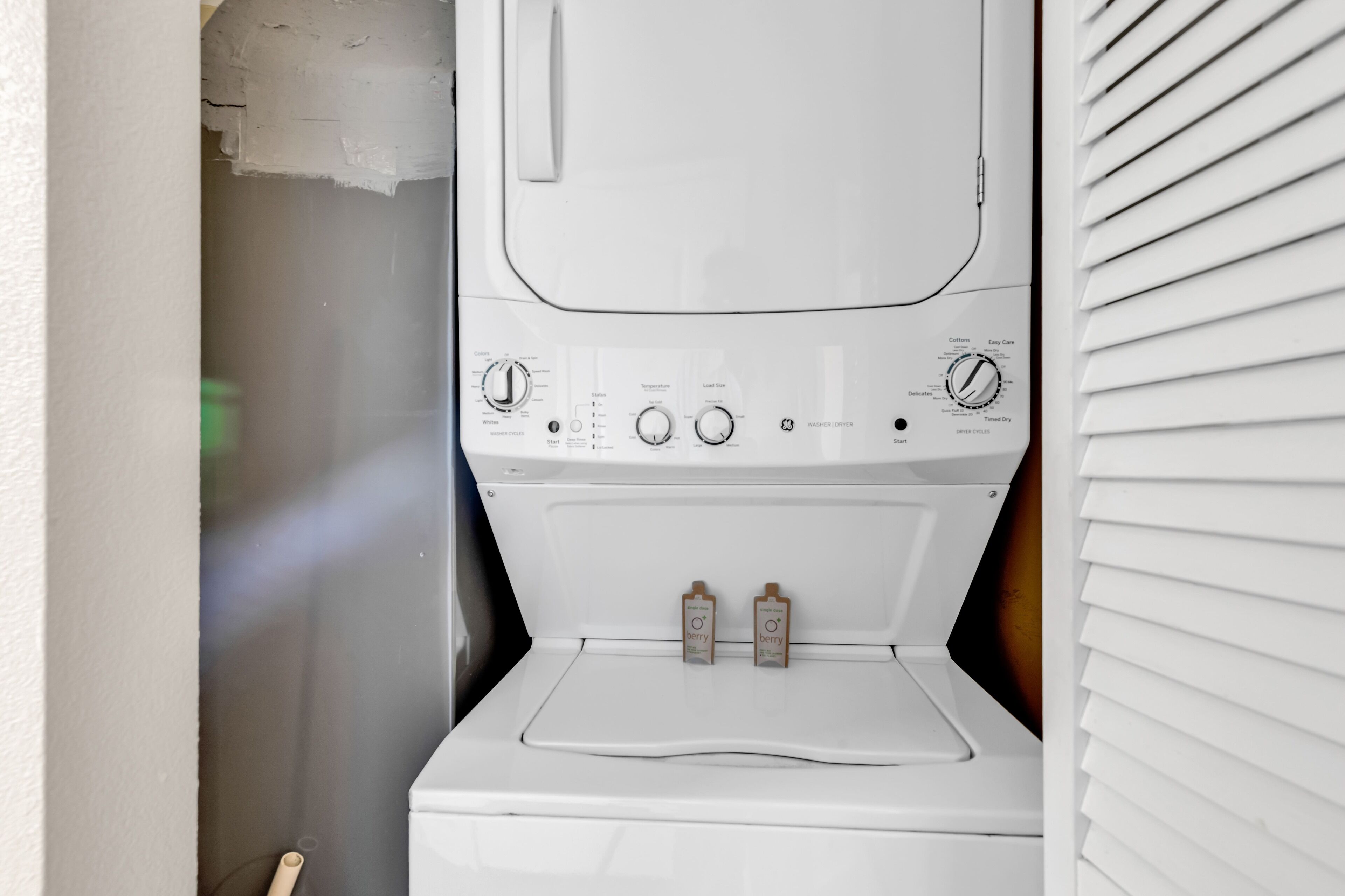 Une machine à laver à chargement frontal, de couleur blanche, dotée de boutons de commande et de deux compartiments à lessive étiquetés « fruits des bois ».
