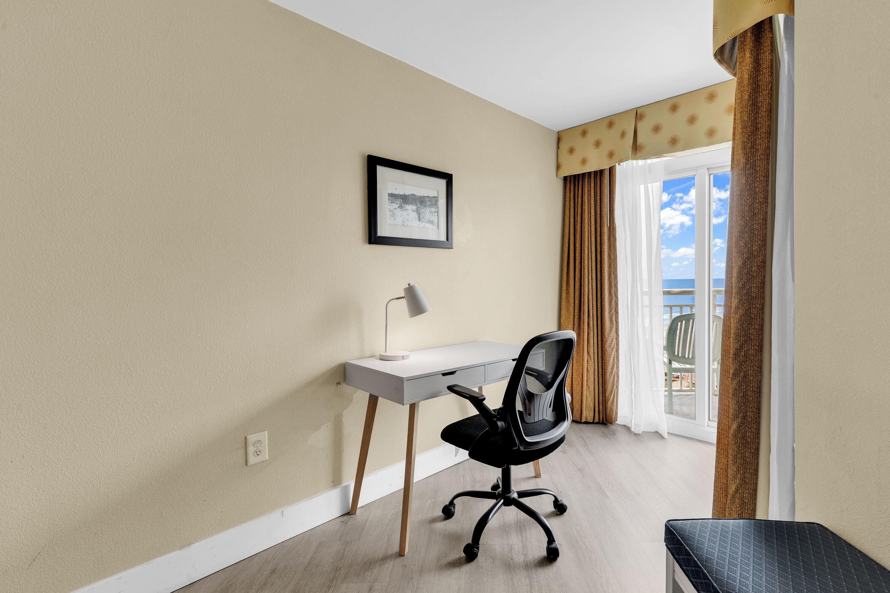 Een kamer met een bureau, stoel en een lijst aan de muur.