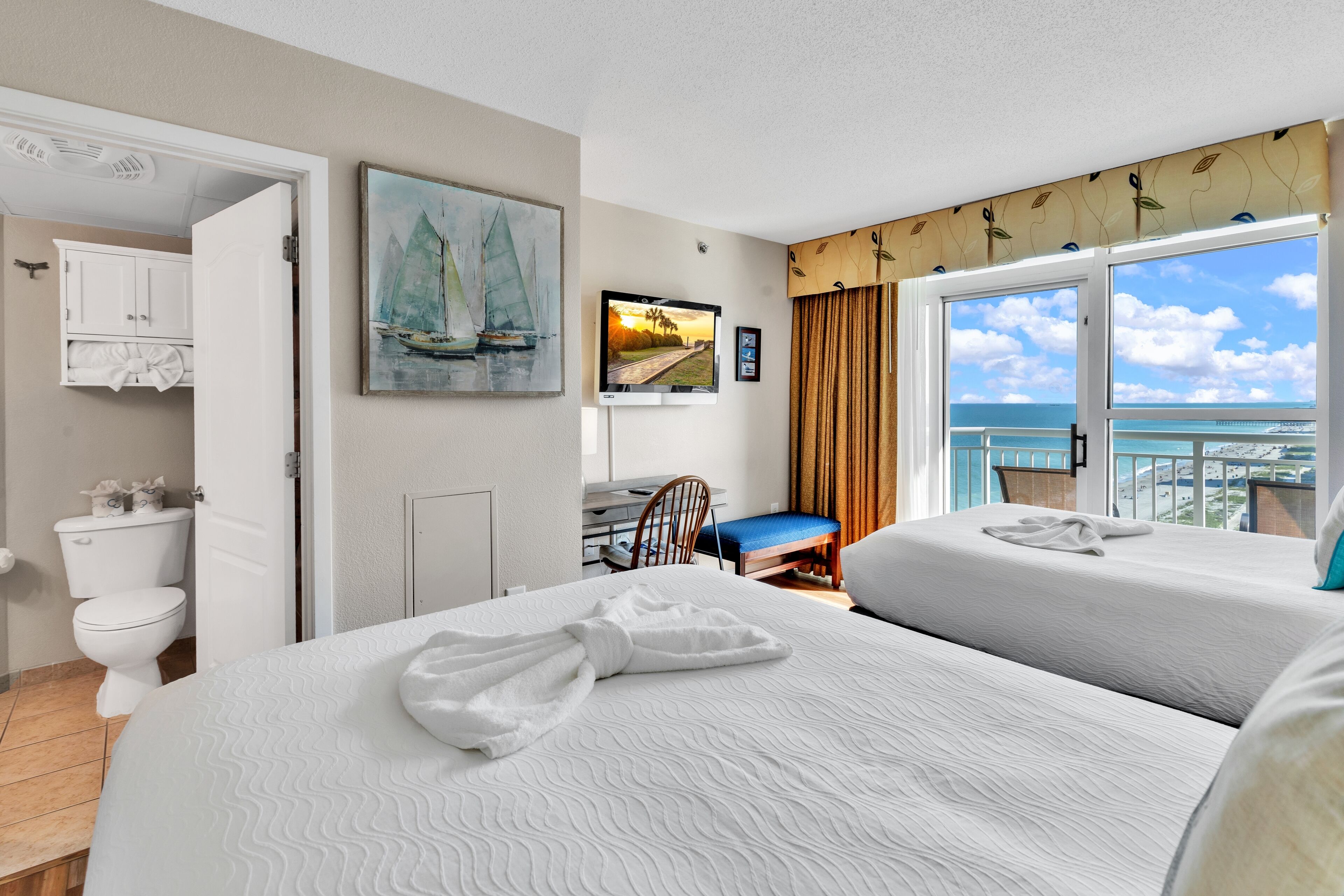 Een hotelkamer met twee bedden, een badkamer, een bureau en een groot raam met uitzicht op de oceaan.