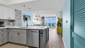 A modern kitchen with grey cabinets, a large island, and a view to the outside. - Carolinian Resort (Myrtle Beach)
