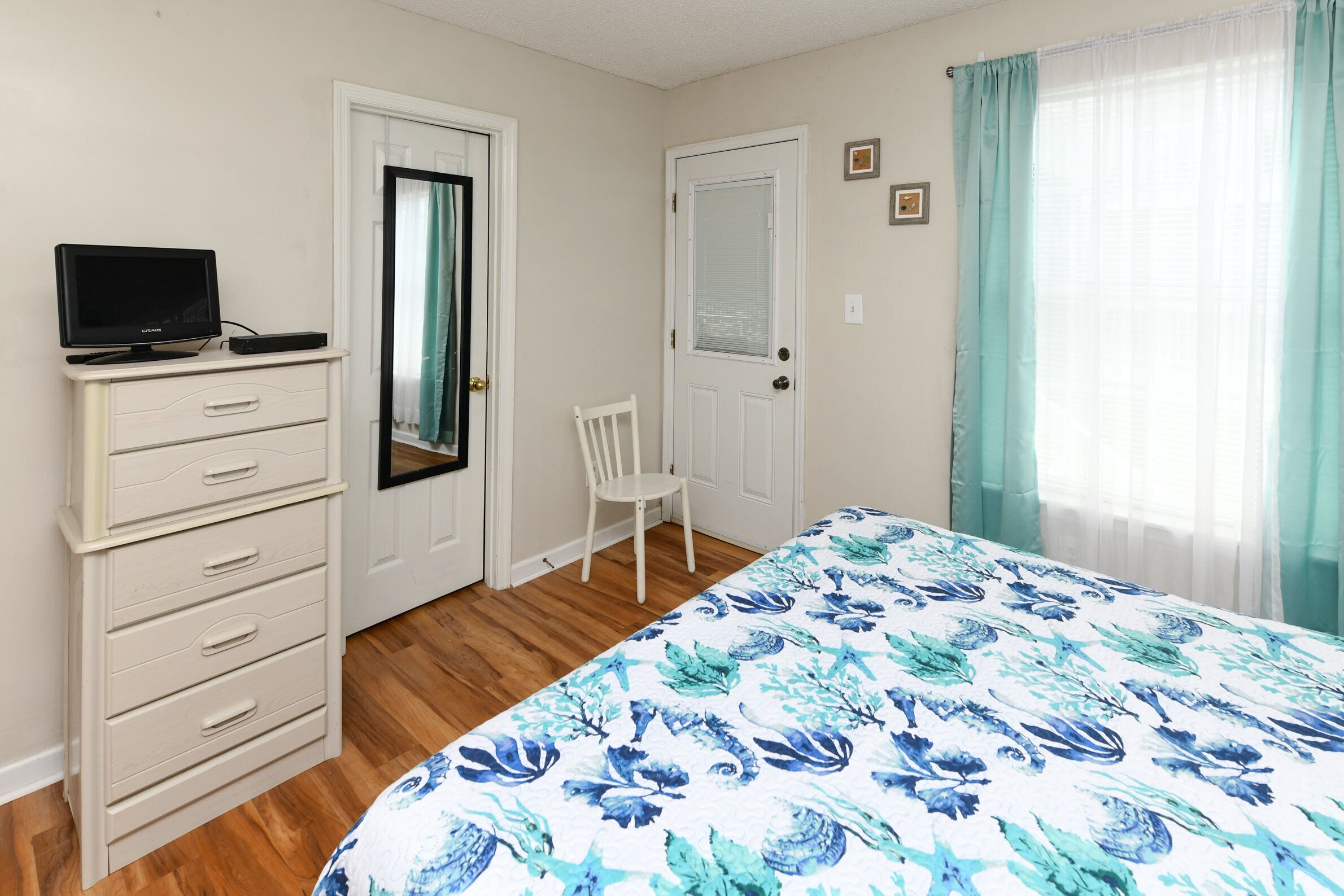 A bedroom with a bed, a dresser, a chair, a television, and two doors.