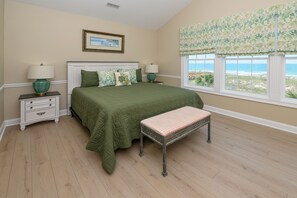 A bedroom with a bed, two bedside tables, a bench, a window with a view, and a framed picture on the wall. - Oceanfront 7 BR Beach House with a Private Pool! Crown Jewel  (Garden City)