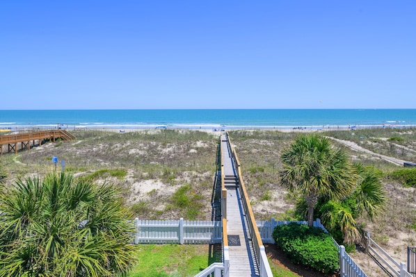A beach boardwalk leading to the ocean with a clear sky.