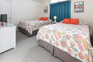 Two single beds with floral-patterned bedspreads and pillows, a wicker dresser, and a television are featured in this cozy room.