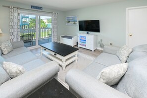 A living room with a sofa set, a coffee table, a television, and a view of the outdoors through a sliding door.