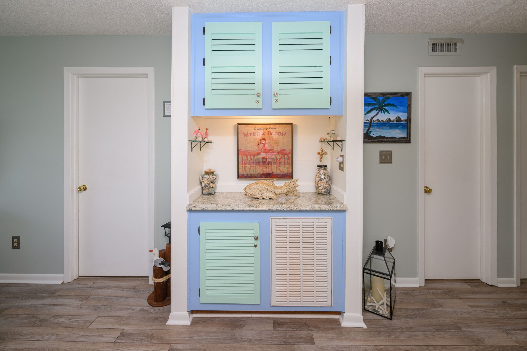A hallway with a blue and white door, a framed picture, and a small shelf with decorative items.