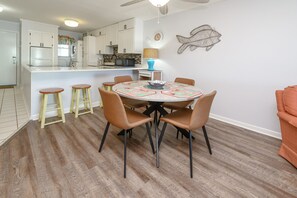 A dining area with a round table, four chairs, and a central island with stools. - 2nd Row 2 BR Condo with a Shared Pool! The Drifter 303  (Garden City)