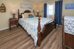 A bedroom with a wooden bed, a nightstand with a lamp, a dresser, and a window with curtains. - 2nd Row 2 BR Condo with a Shared Pool! The Drifter 303  (Garden City)