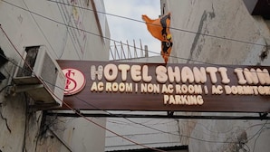 Een bord van Hotel Shanti Inn met reclame voor kamers met en zonder airconditioning, evenals een slaapzaal en parkeergelegenheid.