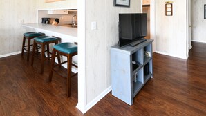 Une cuisine moderne dotée d’un coin bar, de tabourets de bar en bois et d’un téléviseur à écran plat posé sur un meuble.