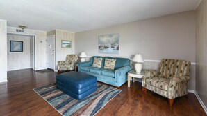 Un salon avec un canapé bleu, des fauteuils à motifs, un pouf bleu et un tapis rayé.