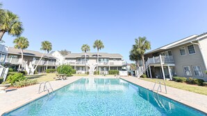 Une piscine entourée d’immeubles d’appartements dotés de balcons et de palmiers.