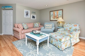 A living room with a striped sofa, a blue armchair, a white coffee table, and a patterned rug. - 2nd Row 2 BR Condo with a Shared Pool! Islander C1 (Surfside Beach)