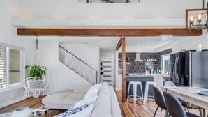 A modern loft-style living space with a high ceiling, exposed wooden beams, a staircase, a kitchen area, and a dining area. - Sea house @ Sea shore - 4 bedroom, 3 bath - 14 ppl (San Diego)
