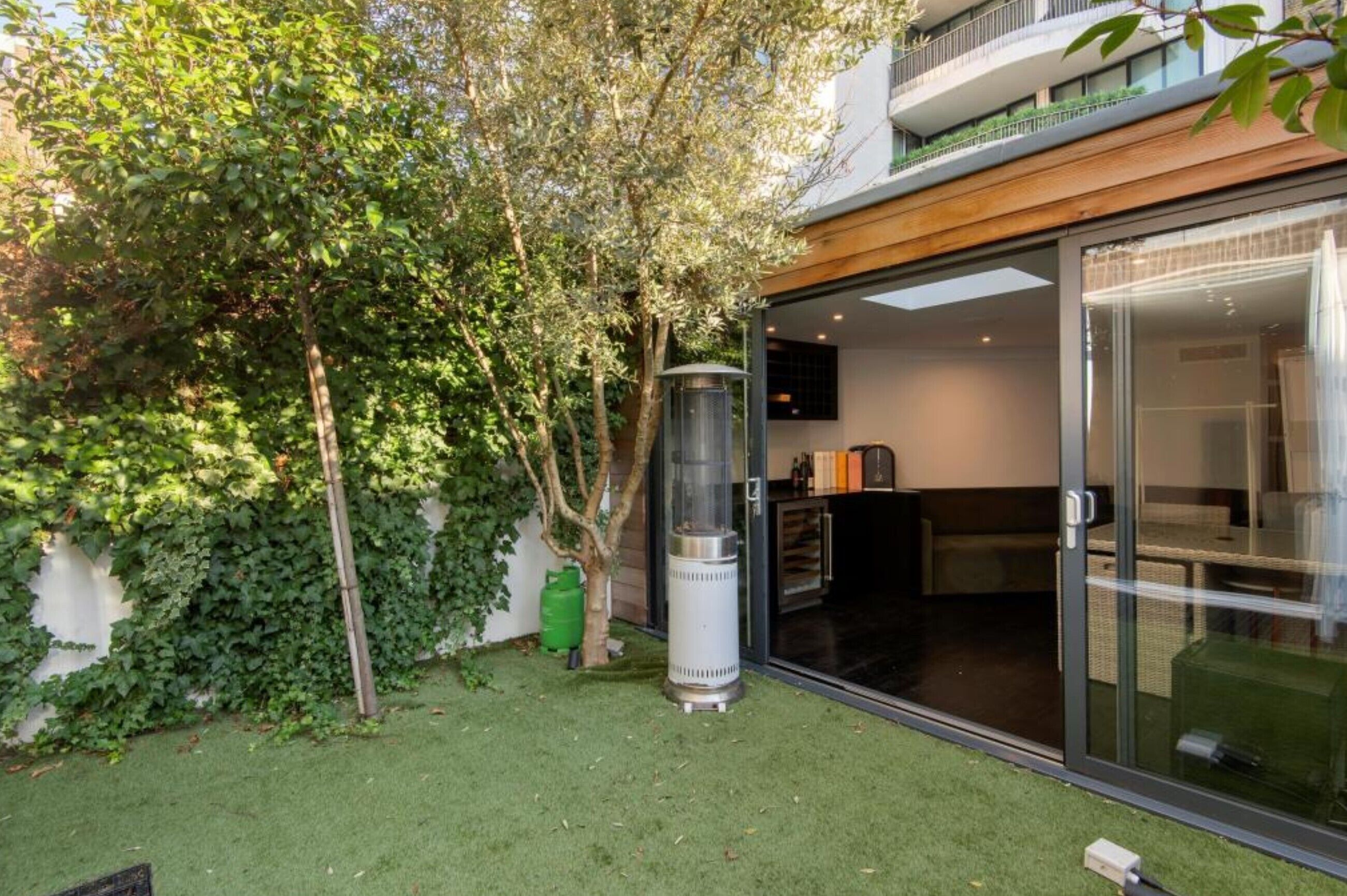 Ein modernes Gebäude mit Glastür, einem kleinen Grill und einem Baum mit üppigem Grün.