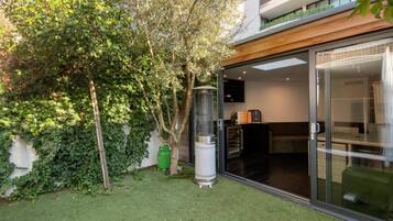 Ein modernes Gebäude mit Glastür, einem kleinen Grill und einem Baum mit üppigem Grün.
