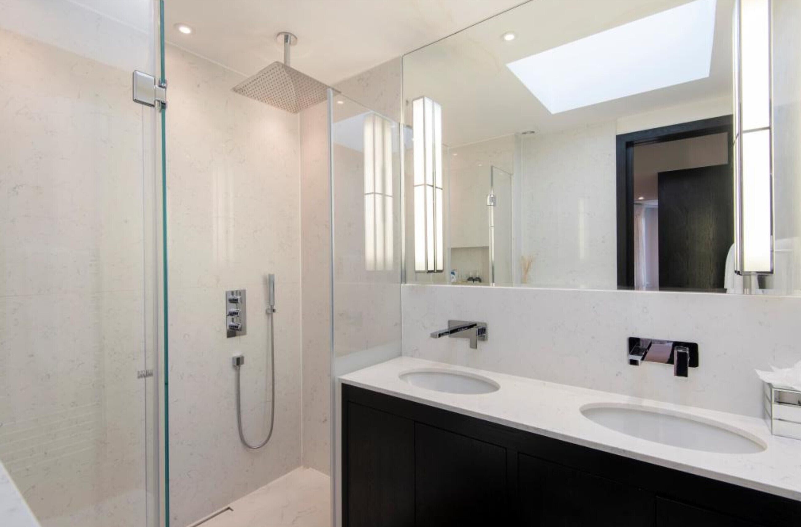 A modern bathroom with a glass-enclosed shower, two sinks, and a large mirror.
