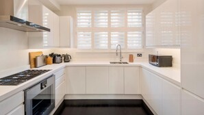 Une cuisine moderne avec des meubles blancs, une cuisinière à gaz, un four à micro-ondes et une fenêtre équipée de stores.