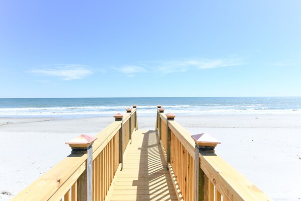 A wooden boardwalk leading to a beach with a clear sky.