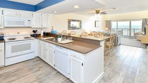 Una cocina moderna con armarios blancos, una isla central y vista al área de estar.