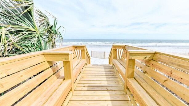 Un muelle de madera que conduce a una playa con palmeras a la izquierda.