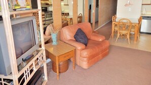 A living room with a leather sofa, a TV, a wooden side table, and a dining area with a table and chairs. - Oceanfront 2 BR Condo with a Shared Pool! Sea Mystique 401   (Garden City)