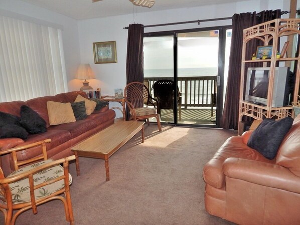 A living room with a leather sofa, a wooden coffee table, a wicker chair, and a television on a wooden stand.